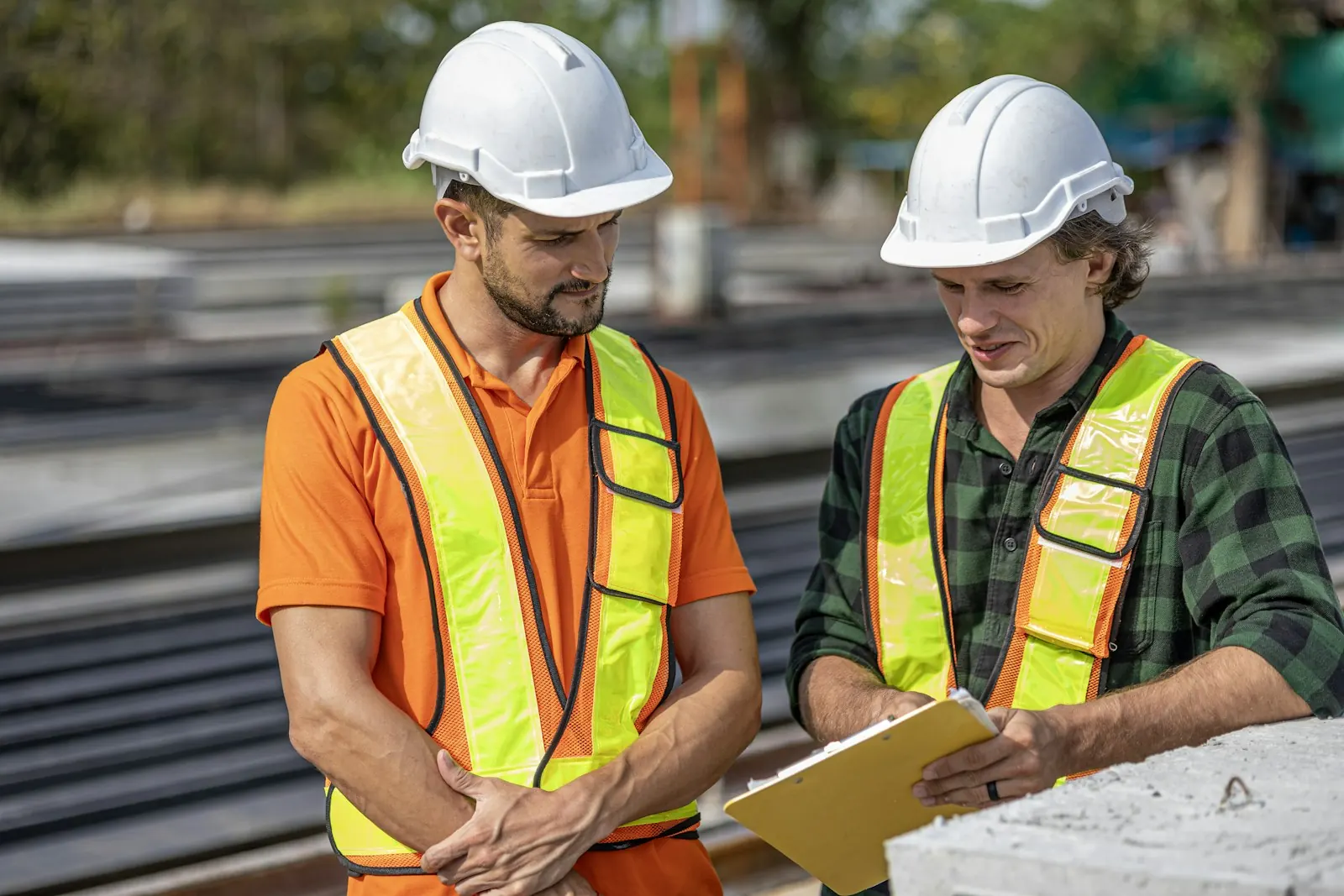 Two safety professionals in hard hats and high-visibility vests reviewing notes on site